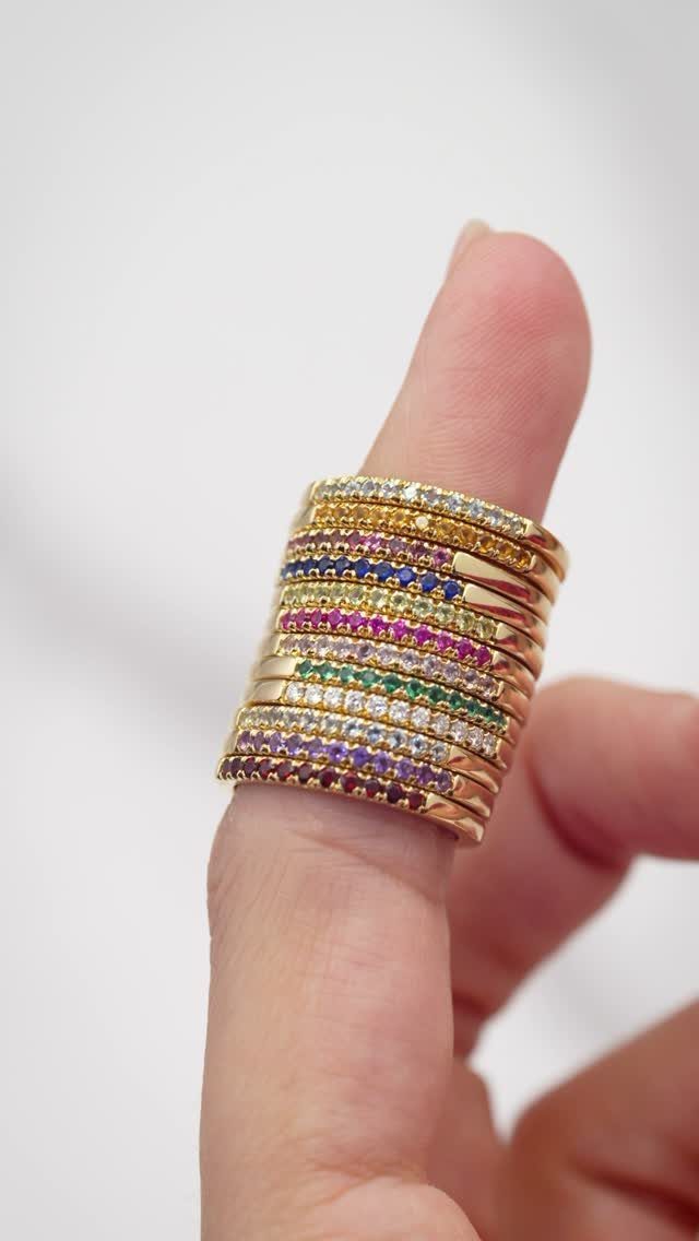 Stack of gold rings with colorful gemstones worn on a person's finger.