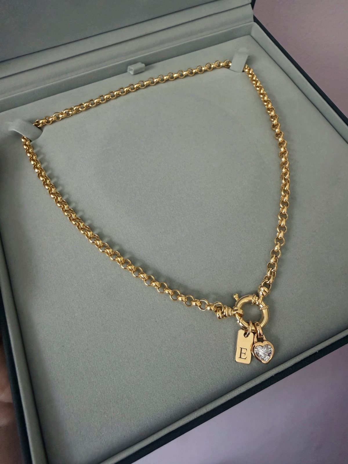 Gold chain bracelet with a letter E charm and heart in a grey box