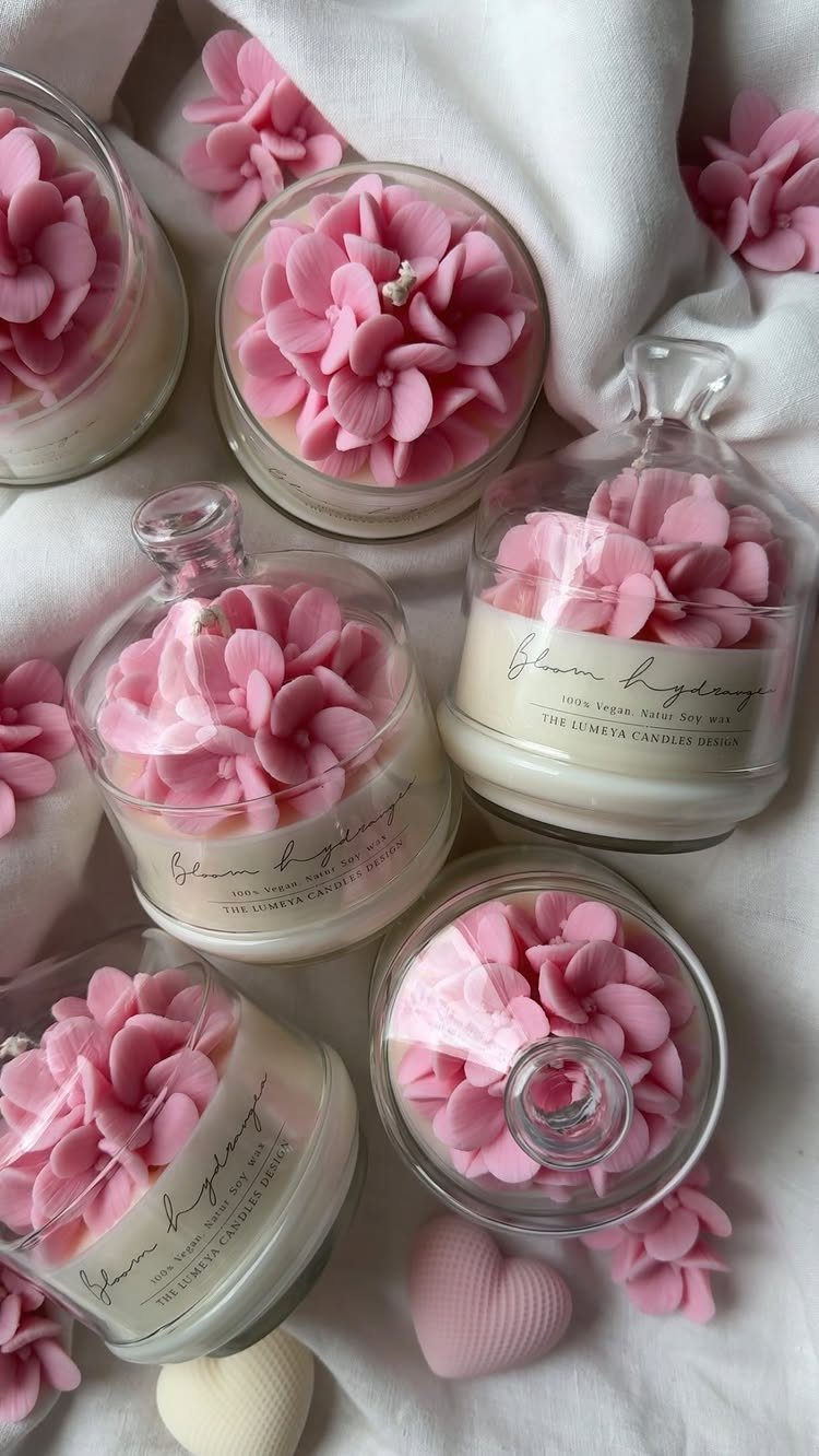 Pink flower wax candles in glass jars on a white fabric background