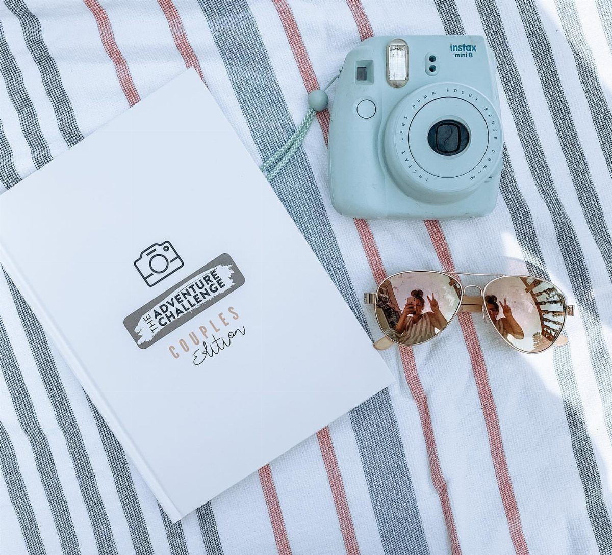 The Adventure Challenge Couples Edition book with a blue camera and sunglasses on fabric