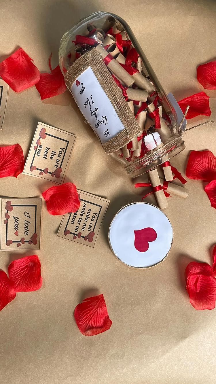 Glass jar filled with rolled love notes and red ribbons surrounded by rose petals