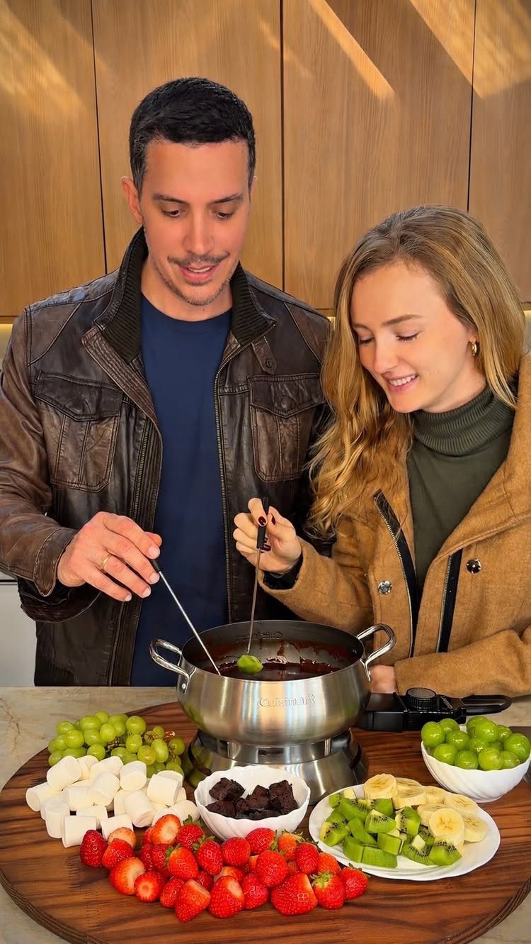 Couple dipping fresh fruit into a chocolate fondue pot on a wooden platter