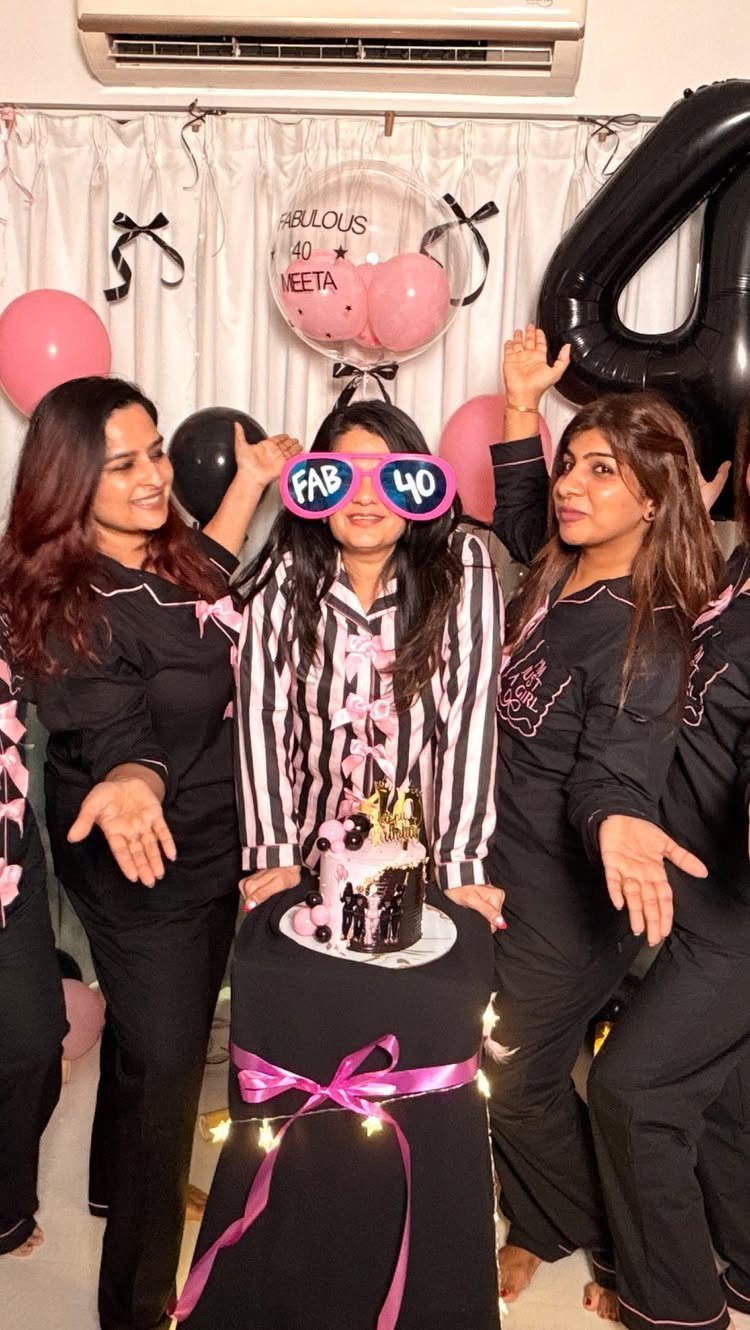 Three women in pajamas celebrating a 40th birthday with balloons and cake.
