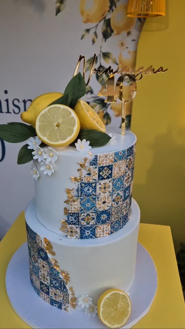 Two-tier white cake with blue tile patterns, lemons, and a gold 40 topper.