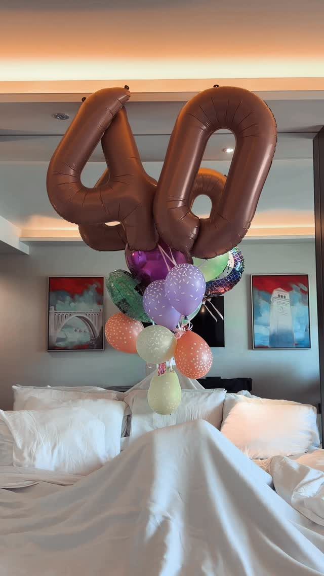 Rose gold number 40 balloons and colorful balloons floating over a white bed.