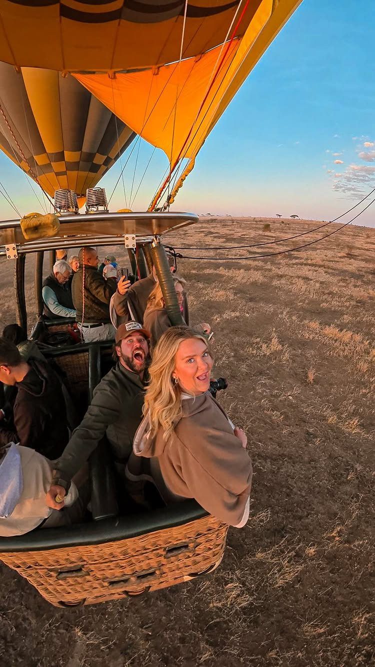 People riding in a hot air balloon over a vast brown savanna landscape.