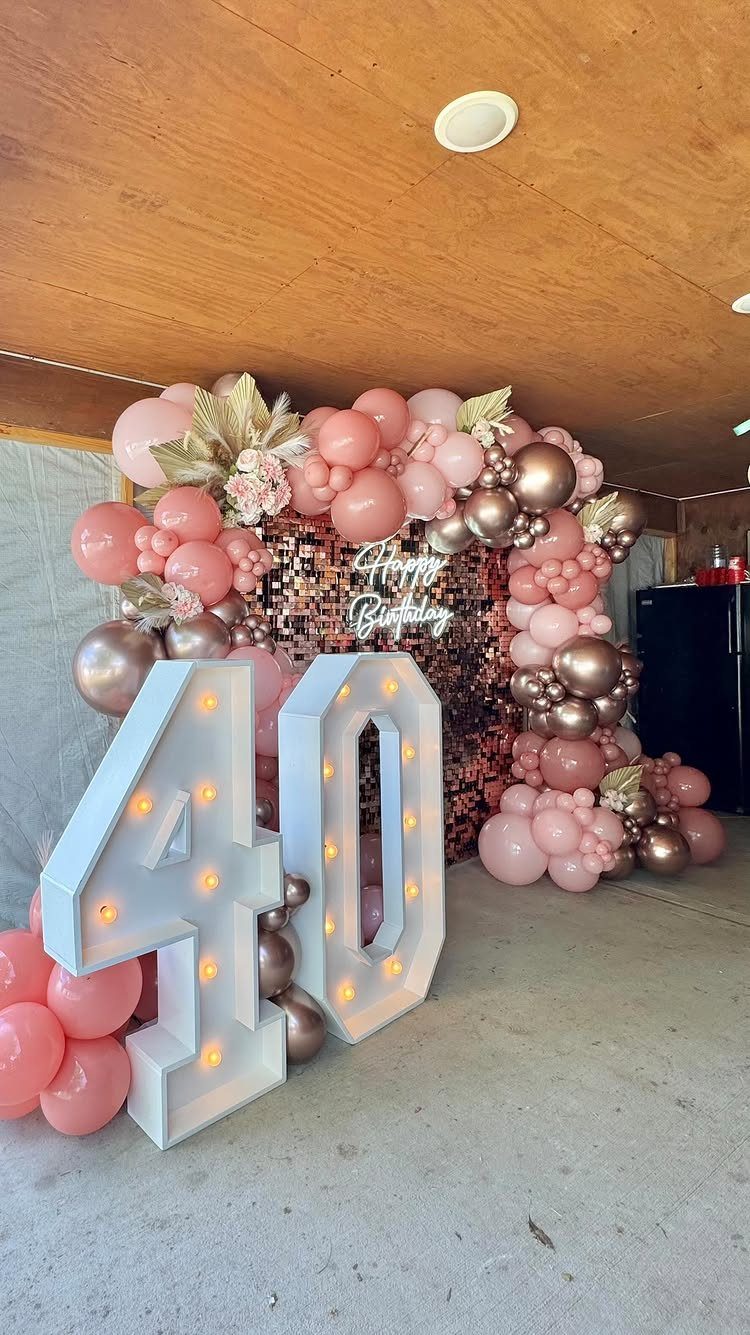 Large illuminated number 40 with a rose gold balloon arch and sequin backdrop.
