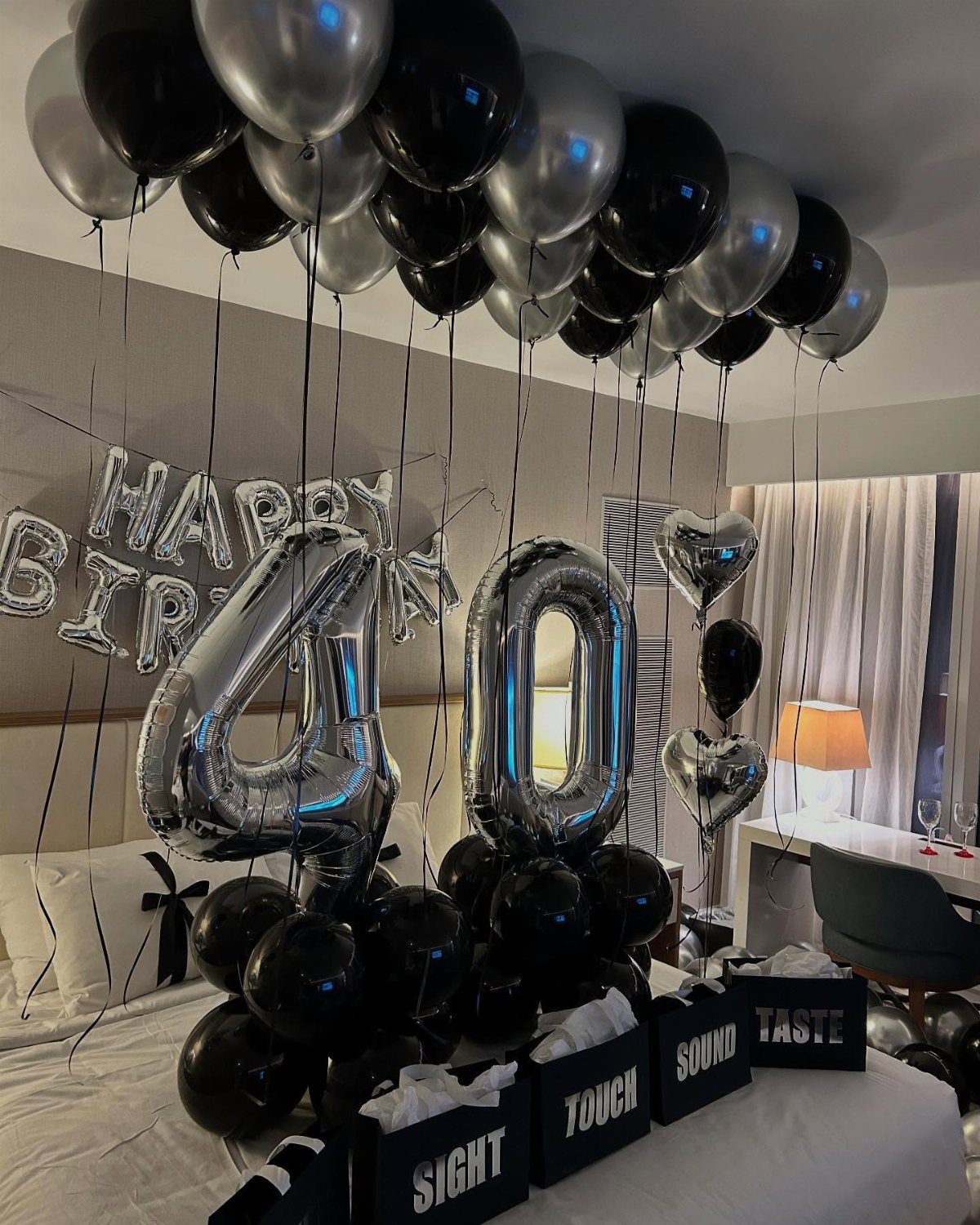 Hotel room decorated with black and silver balloons and a silver 40 balloon.