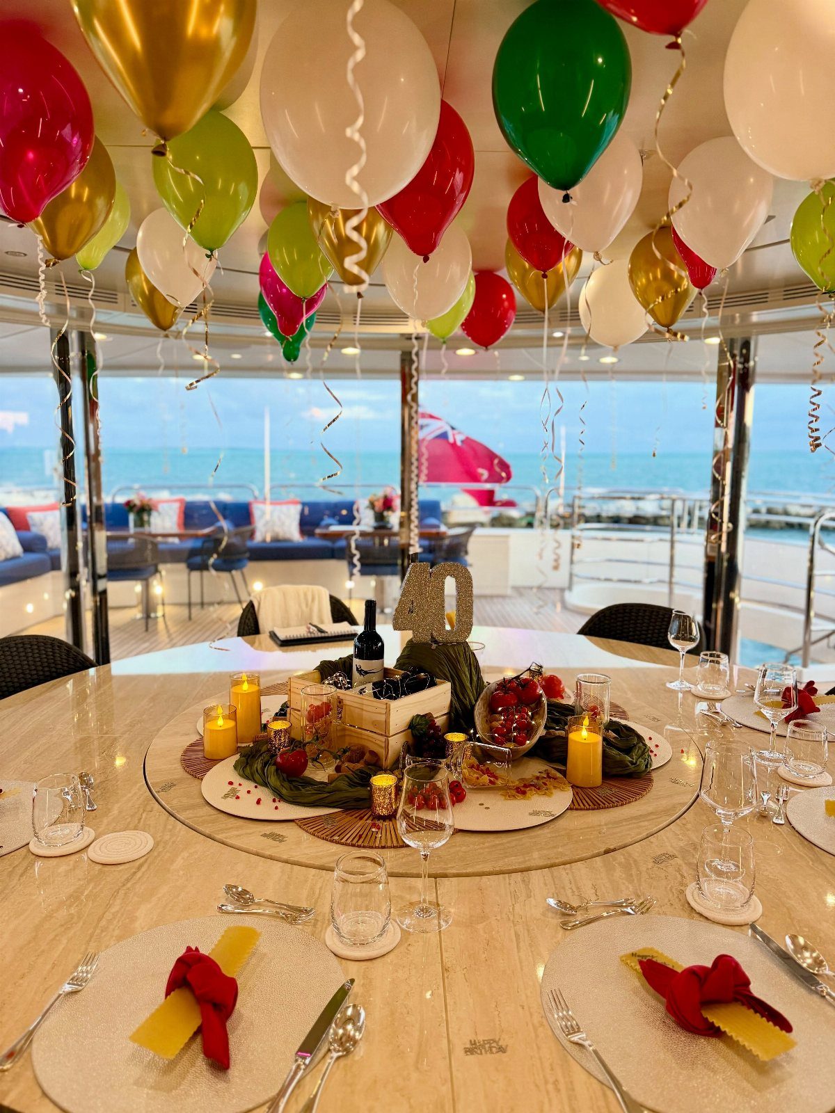 Decorated yacht table with charcuterie, wine, and colorful balloons overlooking the blue ocean.