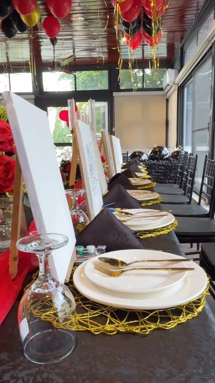 Dining table set with white canvases on easels, gold plates, and red balloons.