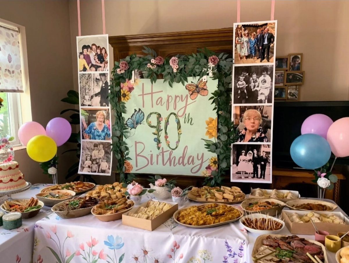 Birthday food table with appetizers, 90th birthday sign, family photos, and colorful balloons.