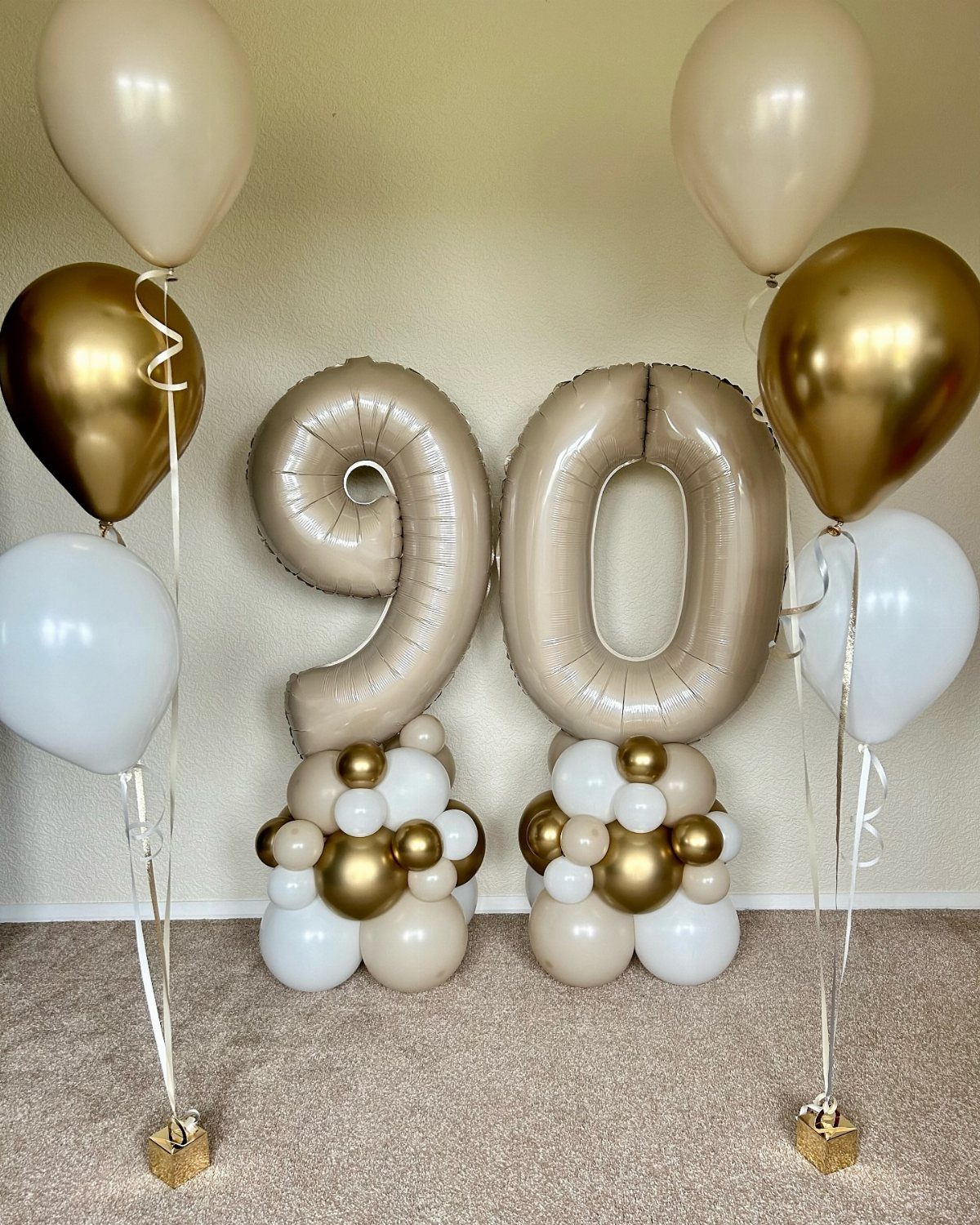 Gold foil number 90 balloons surrounded by white and gold balloon clusters.
