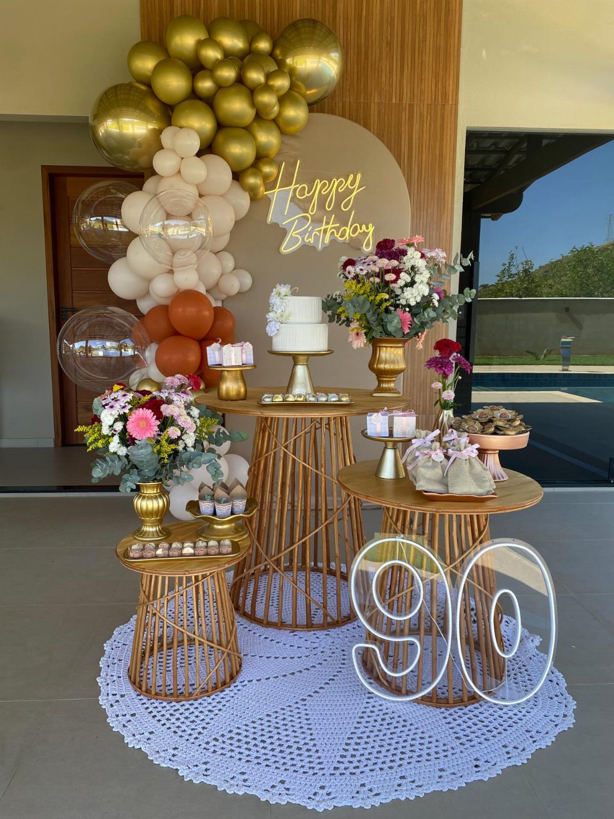 Birthday party decoration with gold balloons, dessert tables, and a glowing number 90.