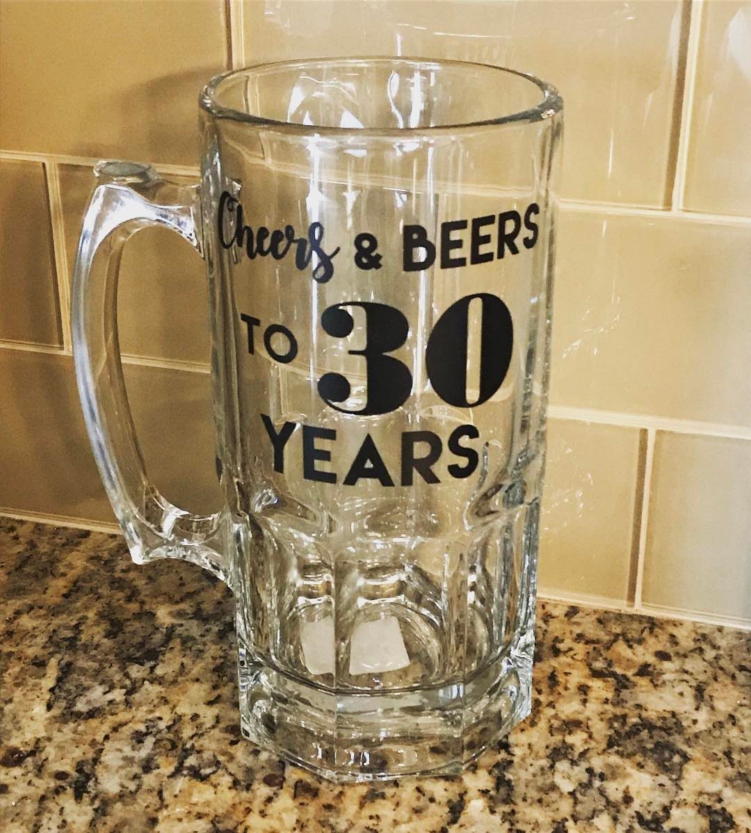 Glass beer mug with black text celebrating 30 years on a granite counter.
