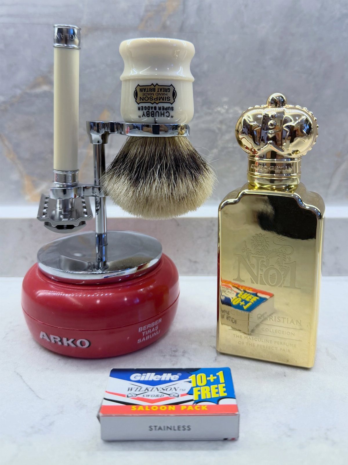 Shaving kit with safety razor, brush, red soap tub, and gold cologne bottle.