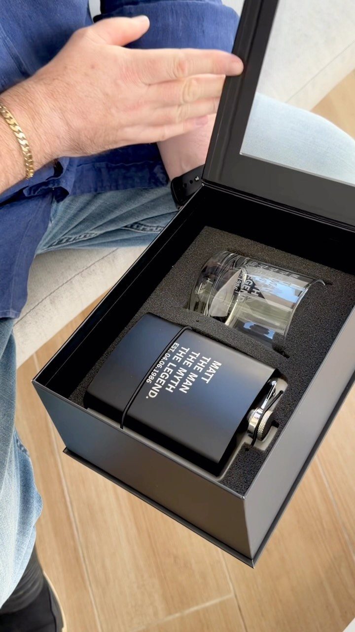 Matte black personalized flask and glass tumbler inside a black gift box.