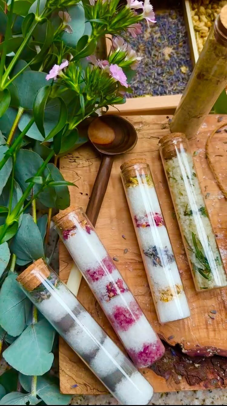 Glass test tubes filled with layered bath salts and dried flowers on wood.