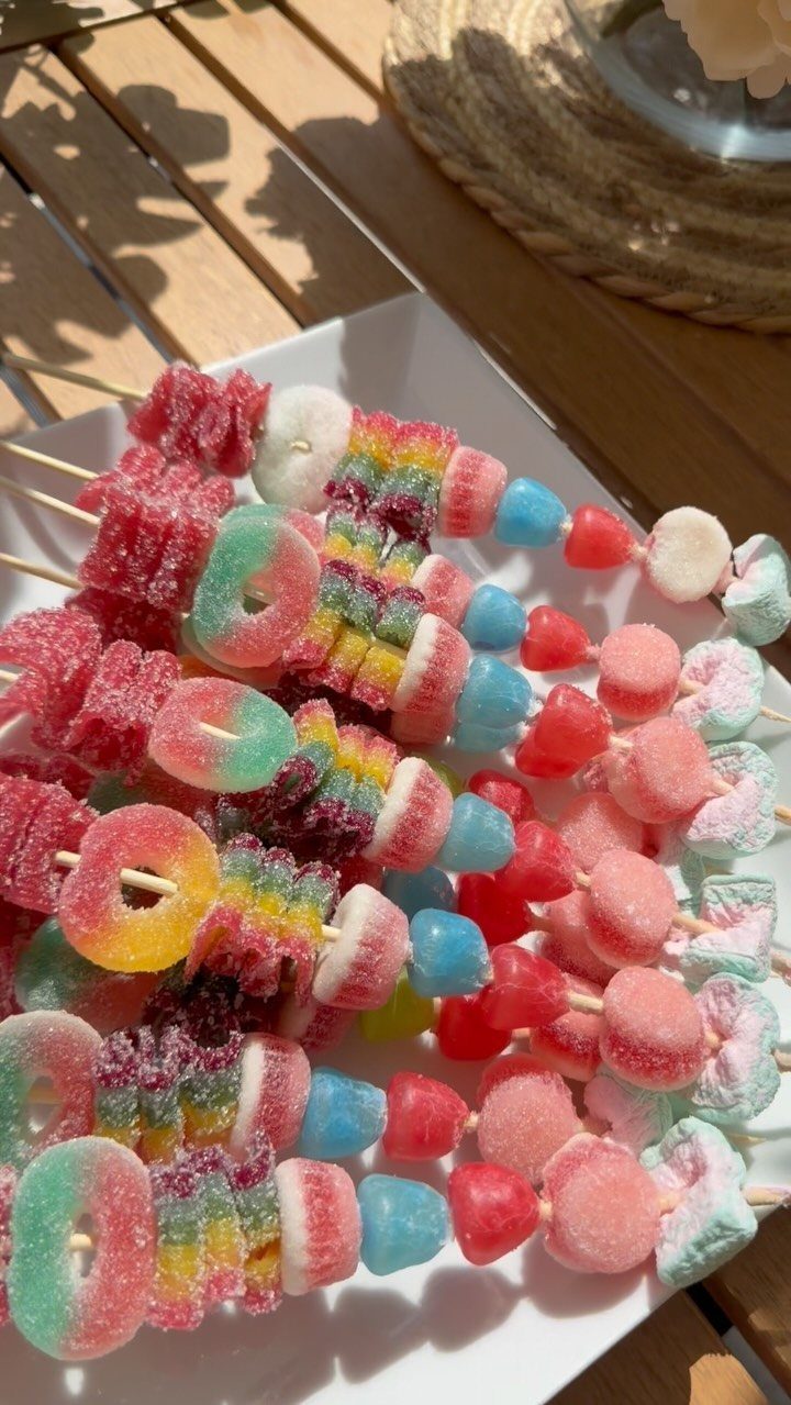 Rainbow sugar-coated gummy candies on wooden skewers arranged on a white platter.