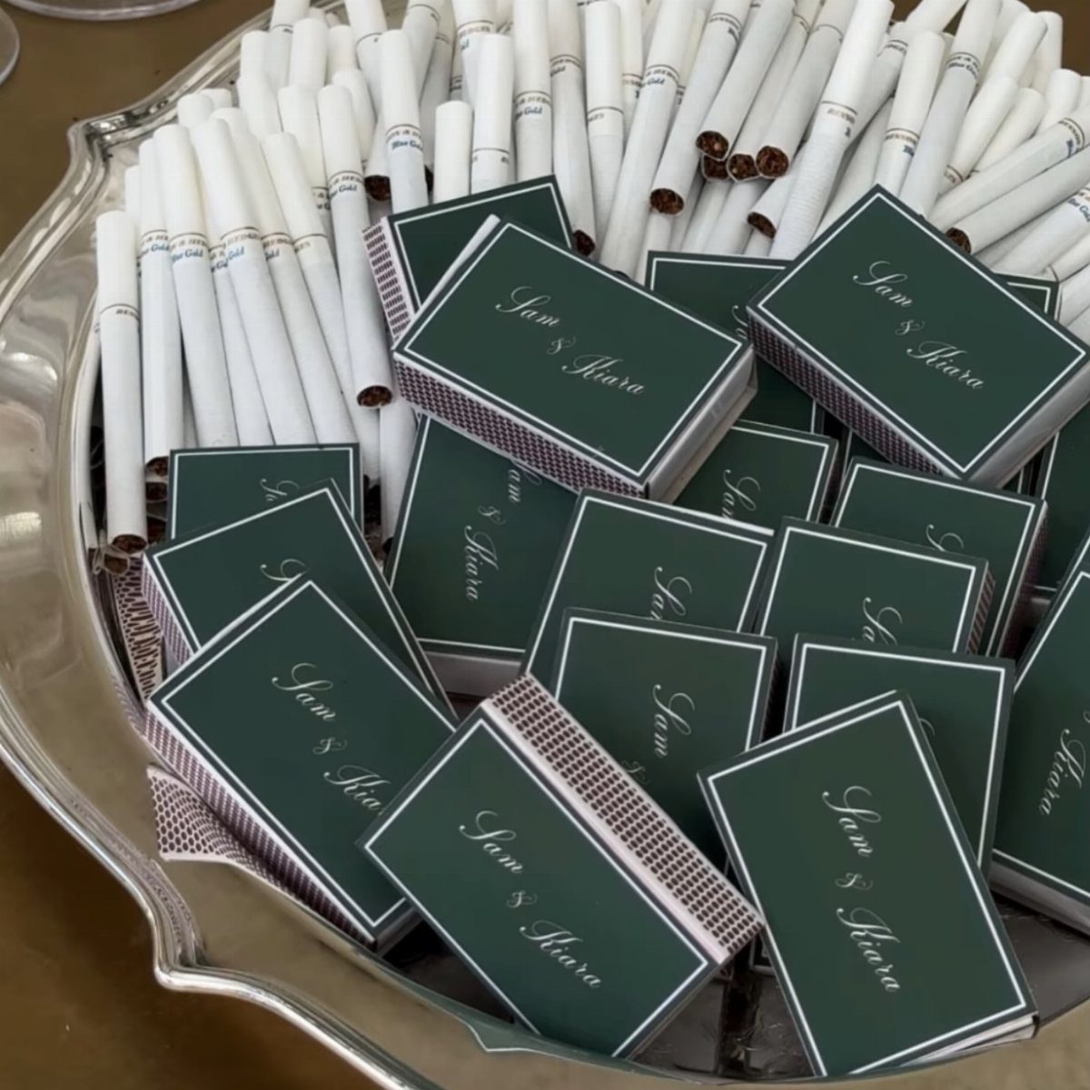 Dark green custom matchboxes with white names resting on a silver tray with cigarettes.