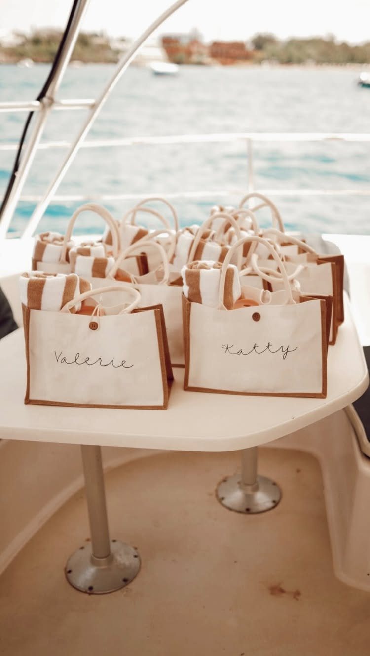 Small white canvas tote bags with personalized names on a boat table.