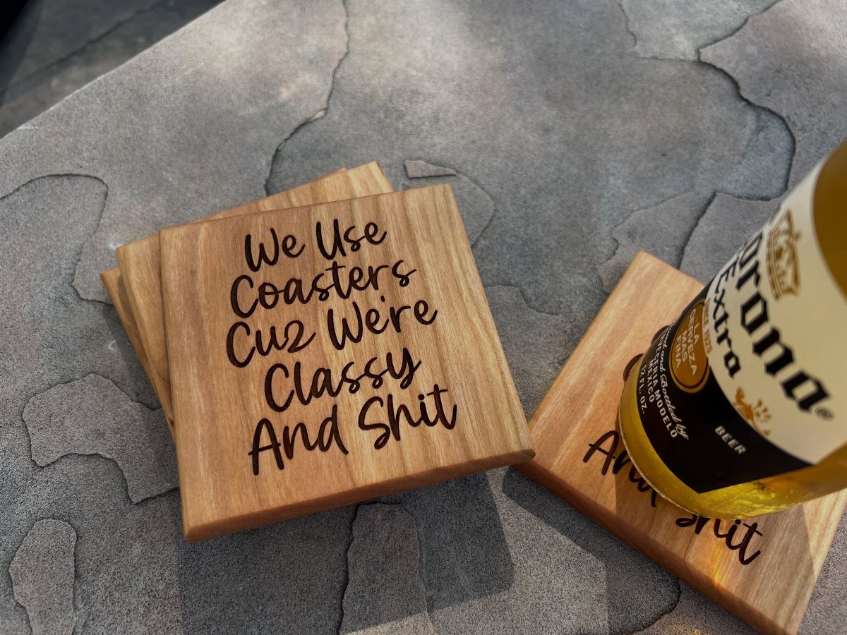 Wooden coasters with funny engraved text and a bottle of beer on stone.