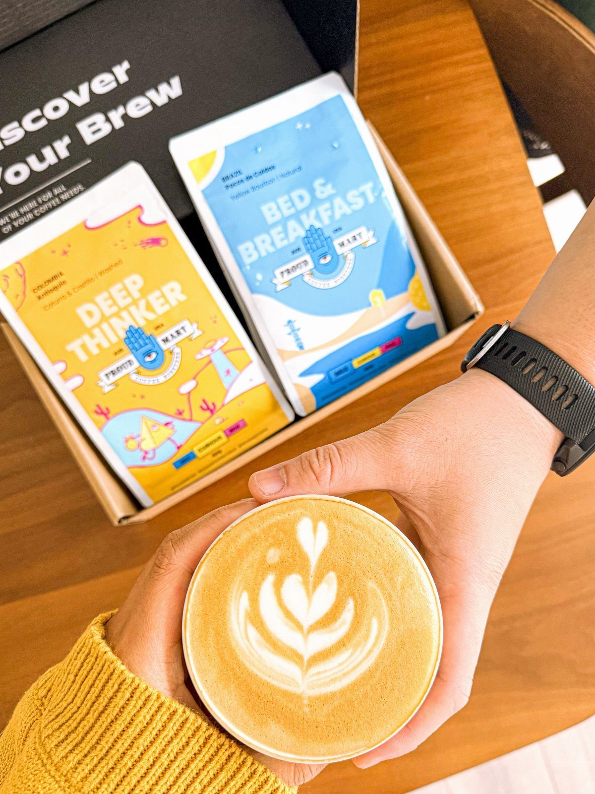 Latte with foam art held in front of a coffee subscription gift box.
