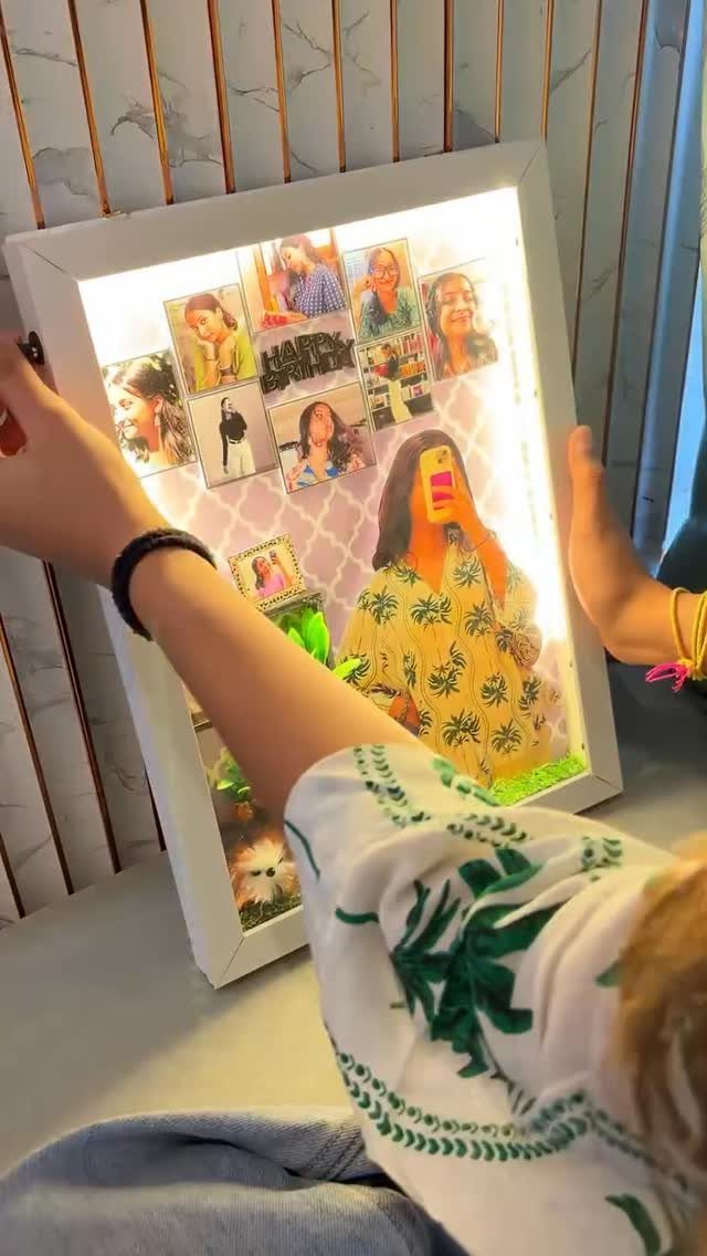 Illuminated white shadow box frame containing a personalized collage of various photographs.