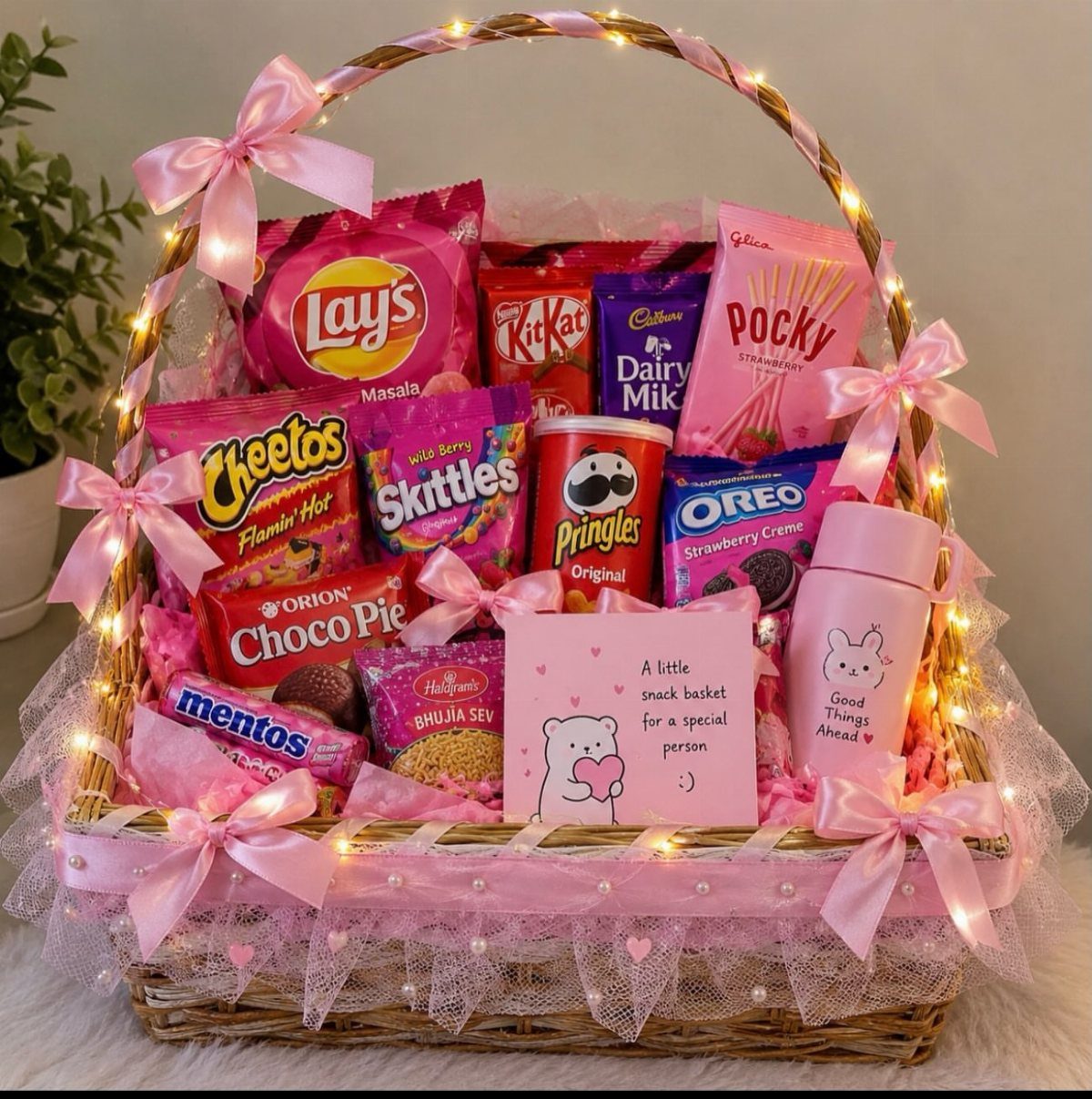 Wicker gift basket filled with assorted colorful snacks and decorated with pink ribbons.