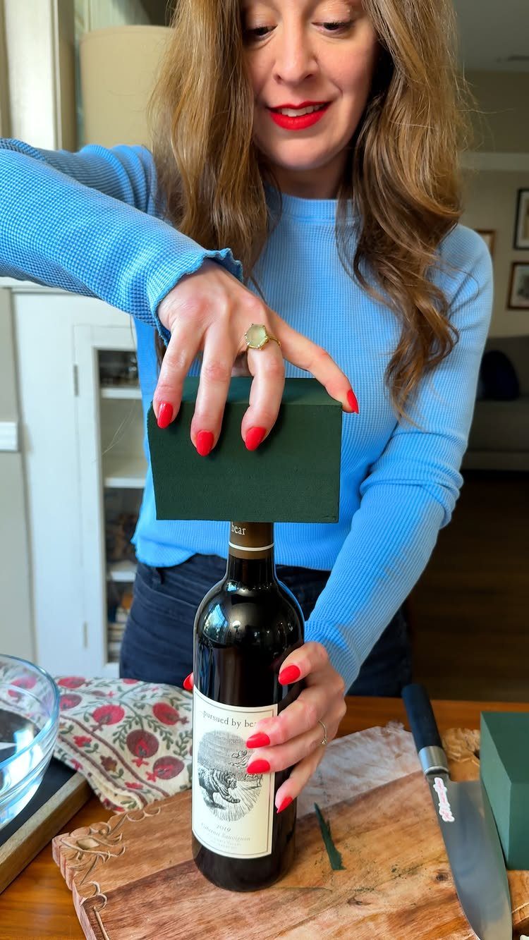 Woman placing a green gift box on a bottle of red wine.