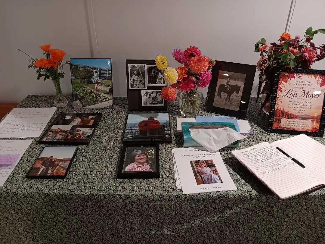 Memorial table with framed photos, colorful flowers, and an open guest book for signatures.