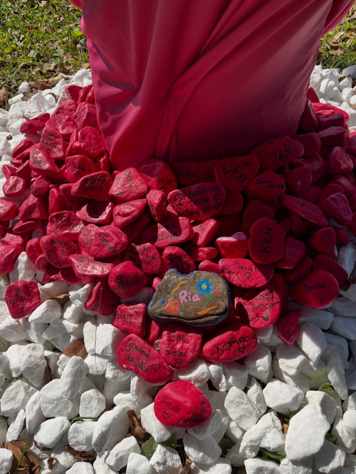 Red painted stones with handwritten messages gathered around a pink draped statue base.
