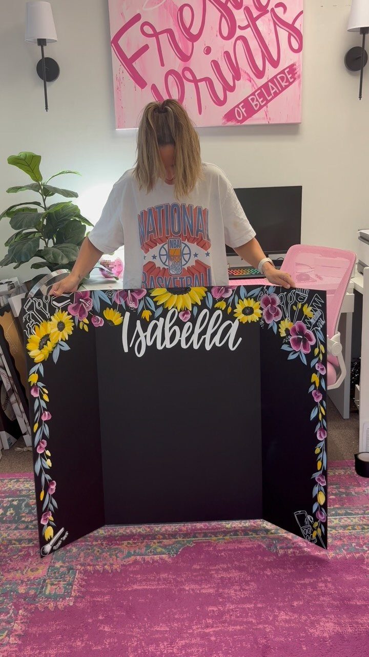 Woman holding a black tri-fold board with floral borders and the name Isabella.
