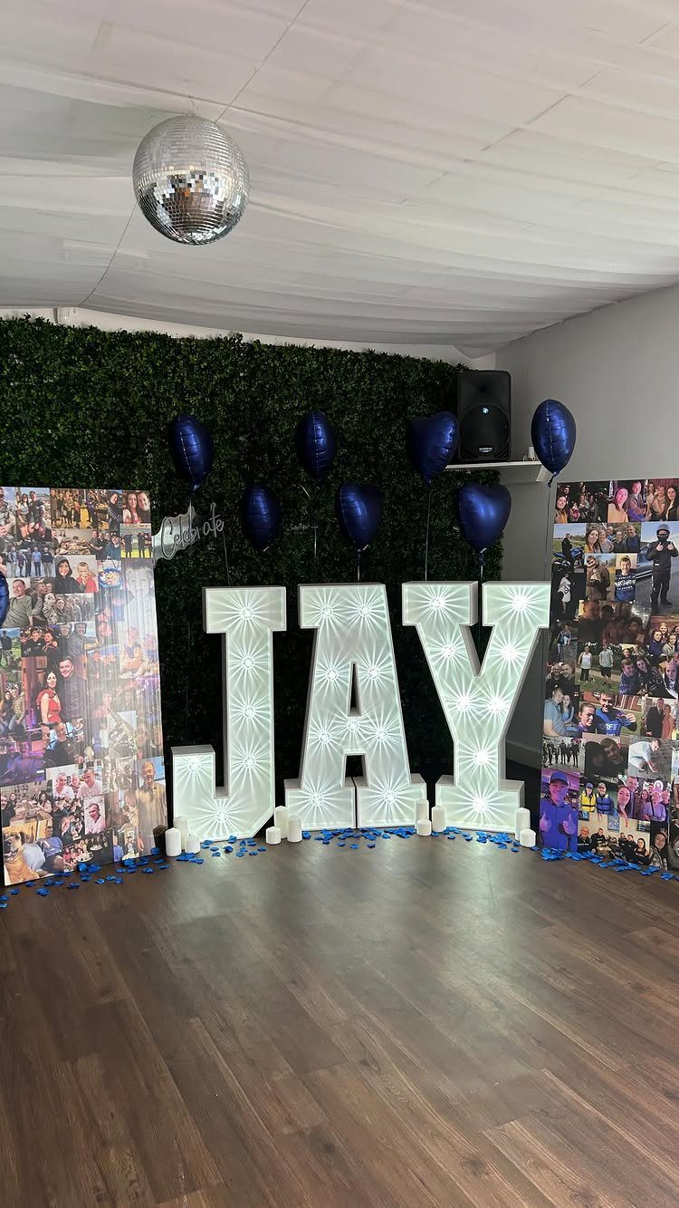 Illuminated letters spelling JAY flanked by two large photo memory collage boards.