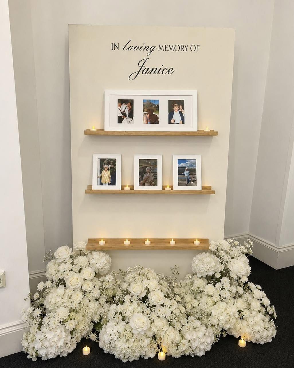 Memorial wall for Janice with framed photos, candles, and white floral arrangements.
