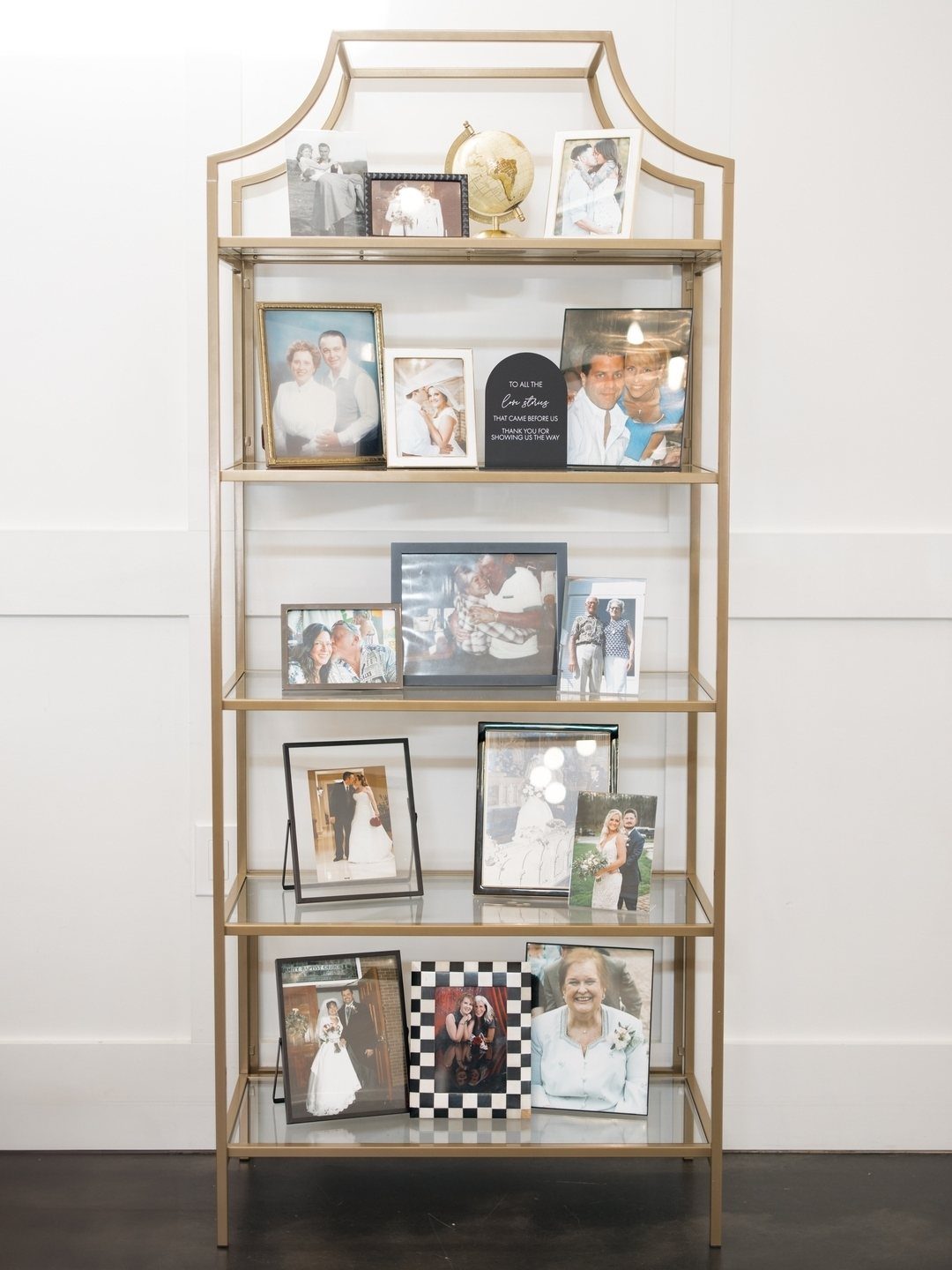 Gold shelving unit displaying framed memorial photographs and a small globe at a wedding.