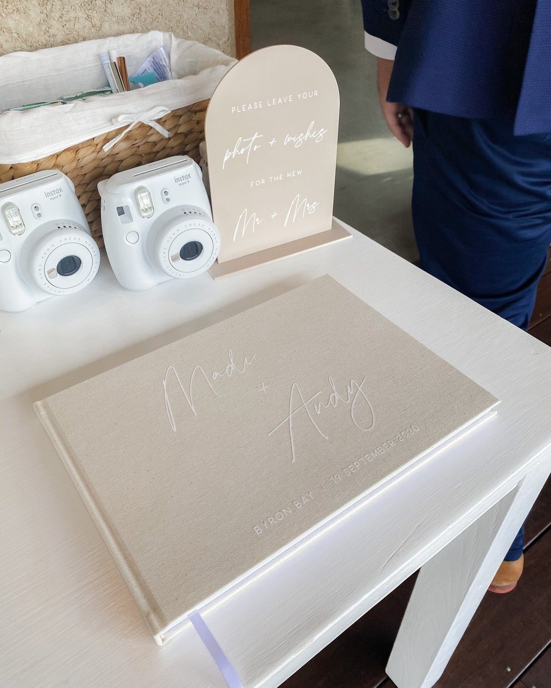 Beige guest book and two white instant cameras on a white wedding table.