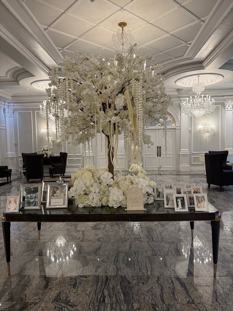 Memory table with framed photos and white flowers under a decorative white tree.