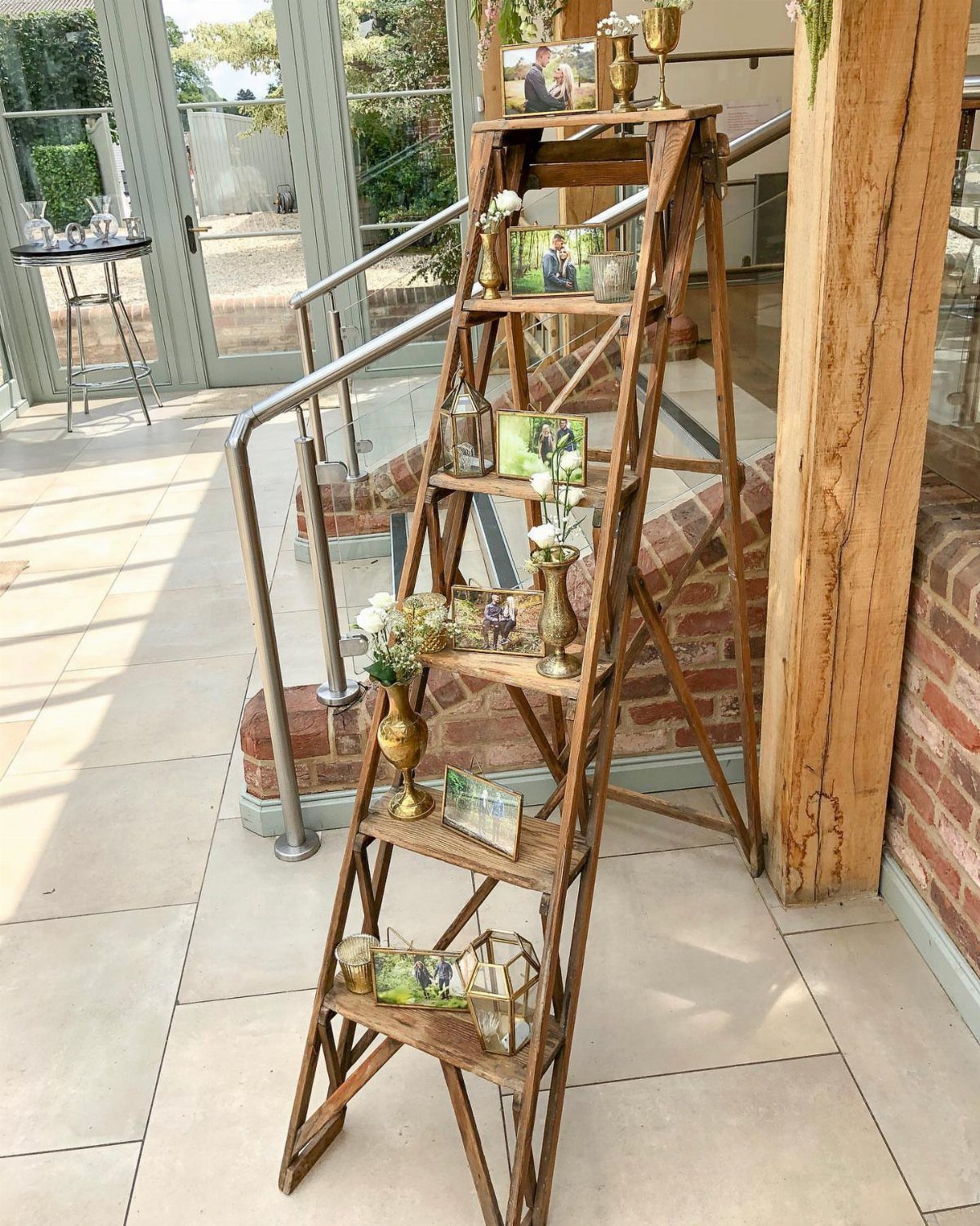 Wooden ladder display holding framed photos, gold vases, and lanterns for a wedding memorial.