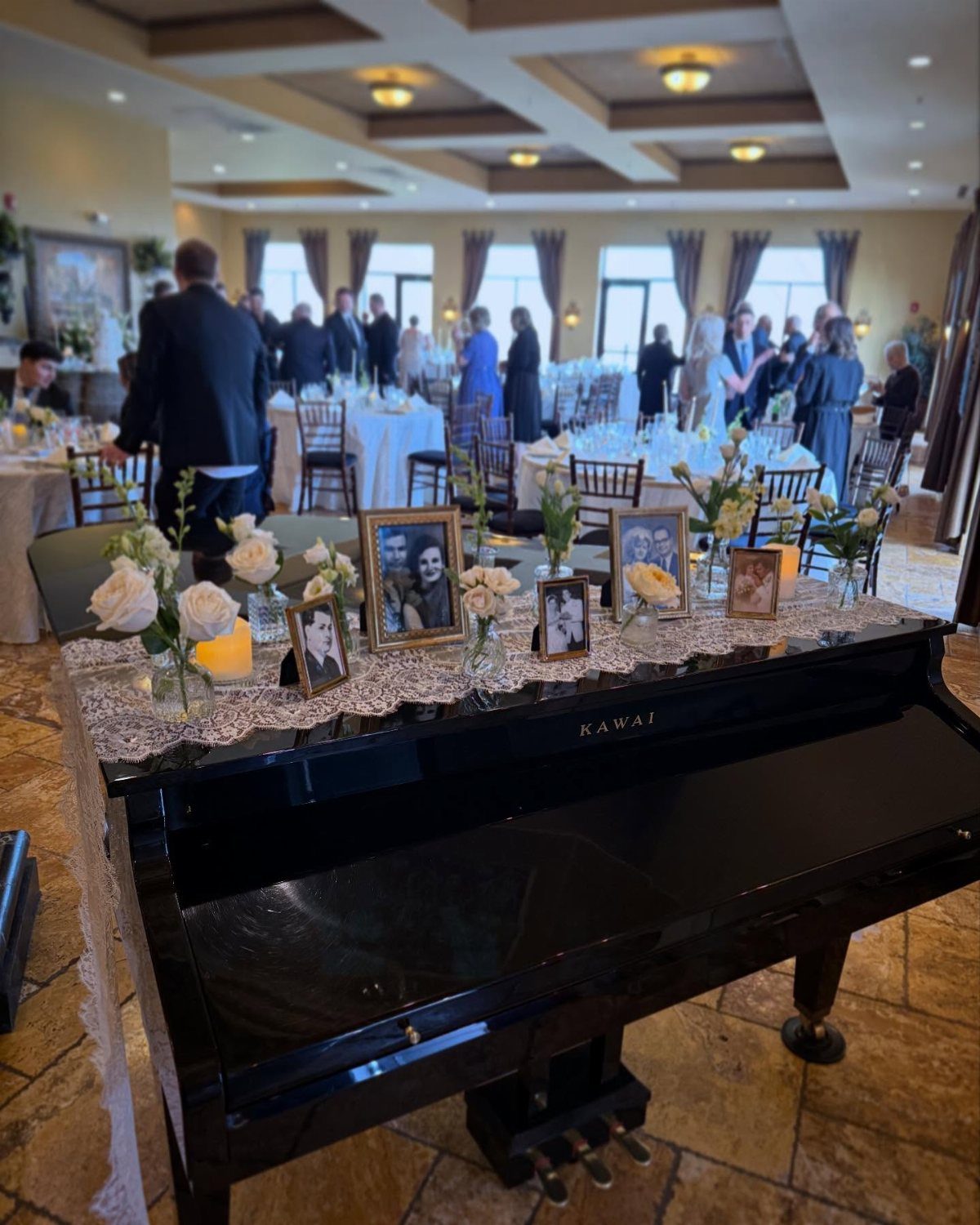 Memory table on a black piano with framed photos, white flowers, and candles.