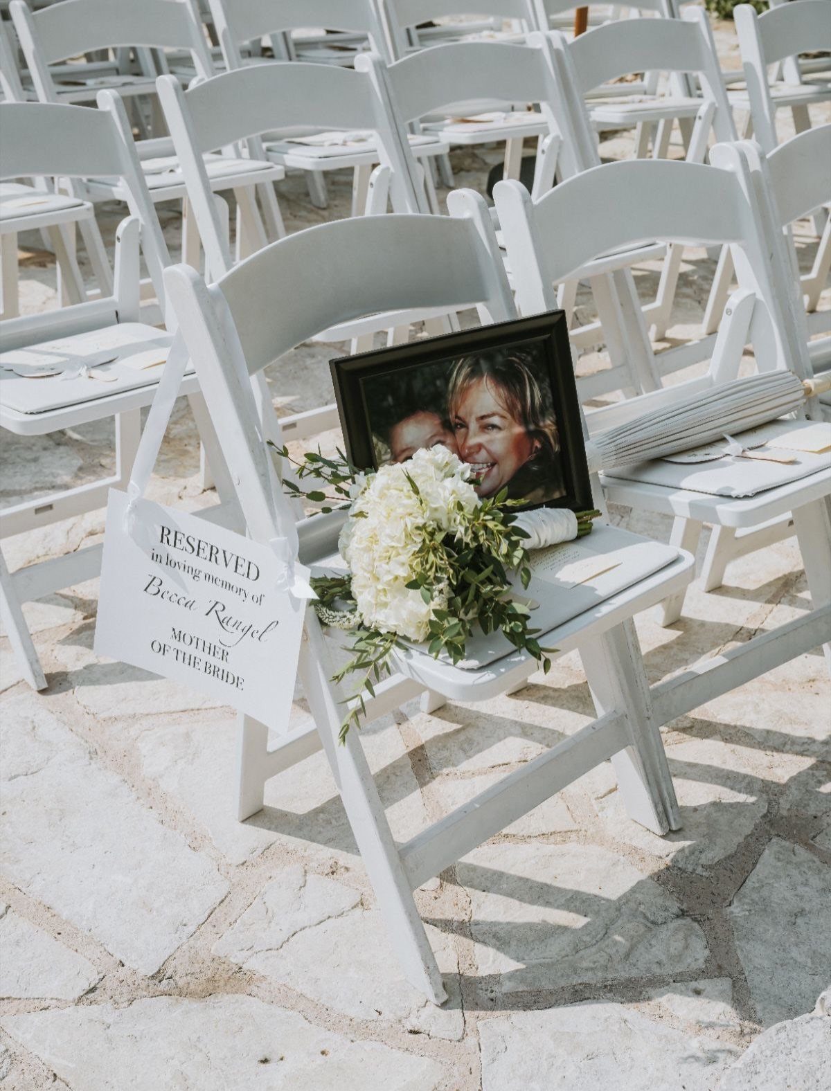Reserved wedding chair with a framed memorial photo and white floral bouquet.