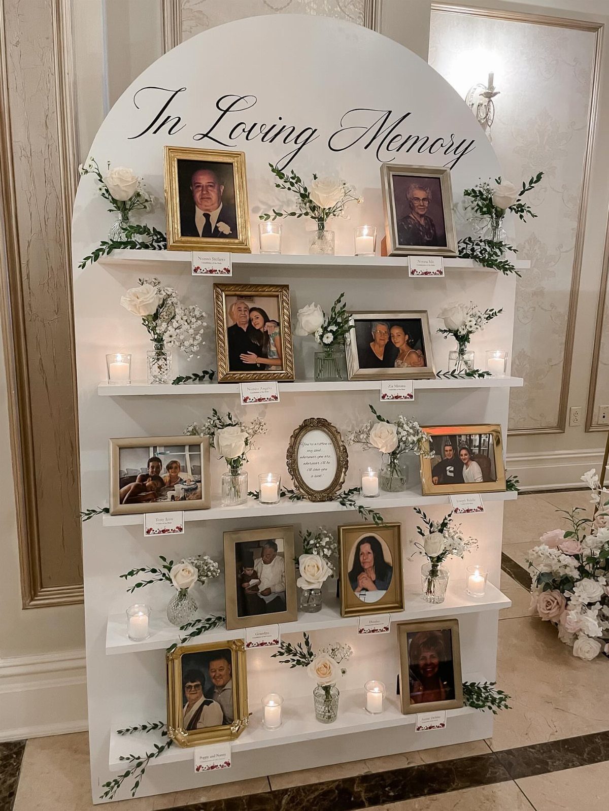 White arched memory table with framed photos, white flowers, and candles for a wedding.