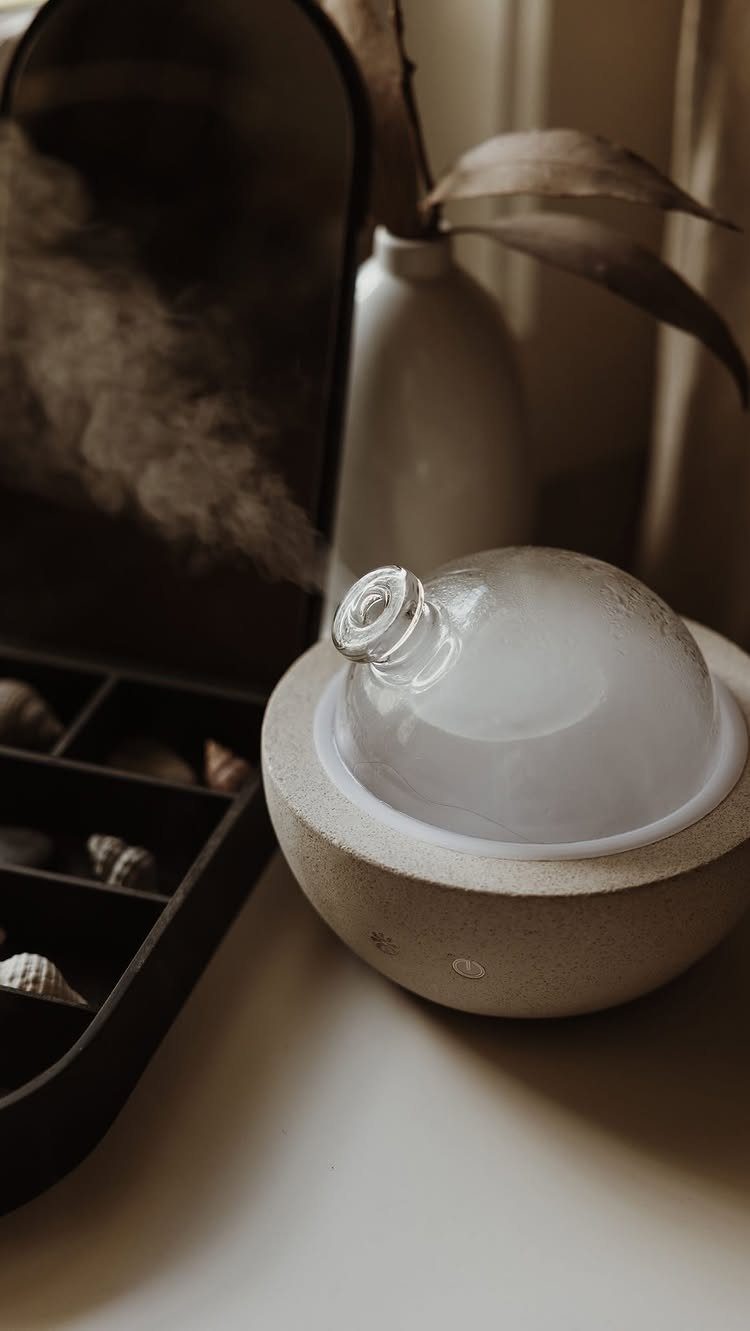 Ceramic aromatherapy diffuser with a glass dome emitting white mist on a table