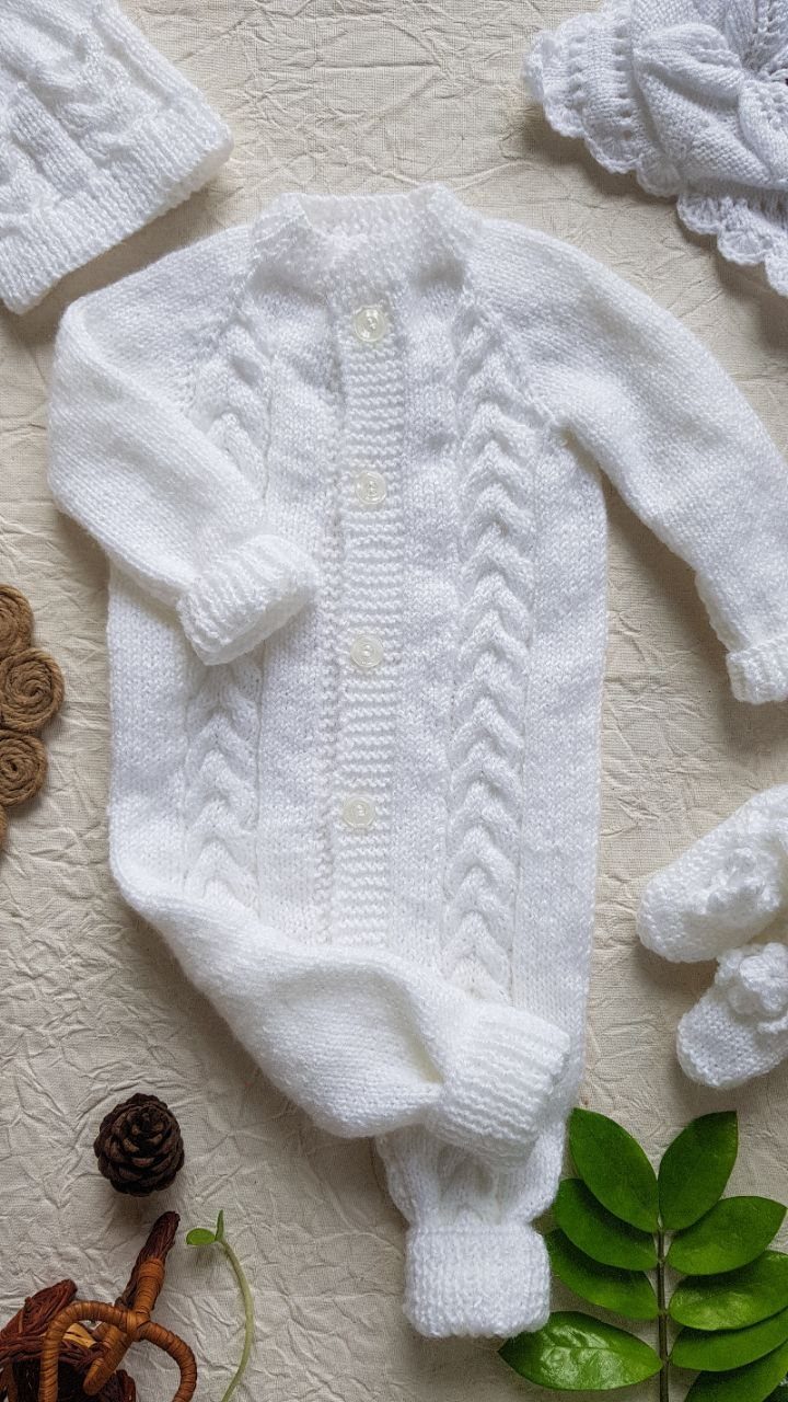 White knitted newborn baby romper with matching hat and booties on beige background