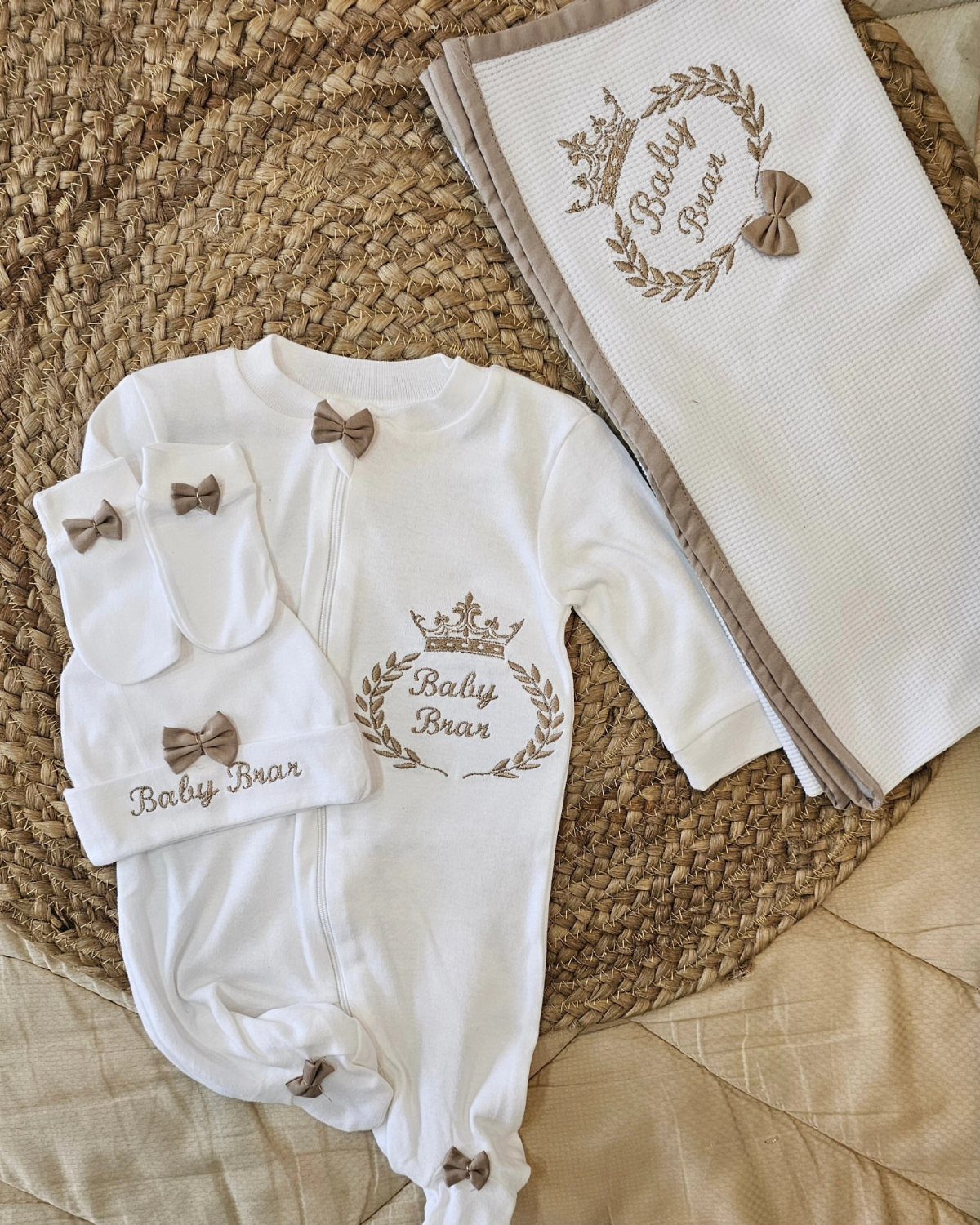 White newborn onesie set with matching hat, socks, and swaddle on jute mat