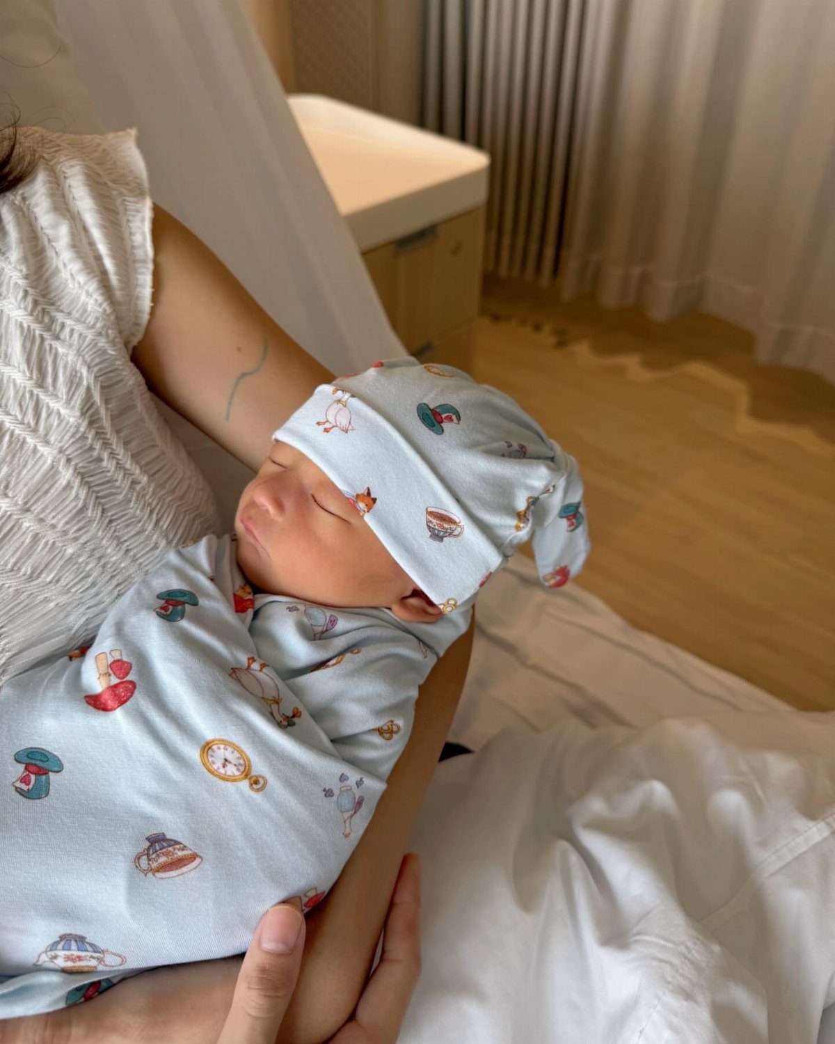 Newborn baby sleeping in a light blue patterned swaddle and matching hat.