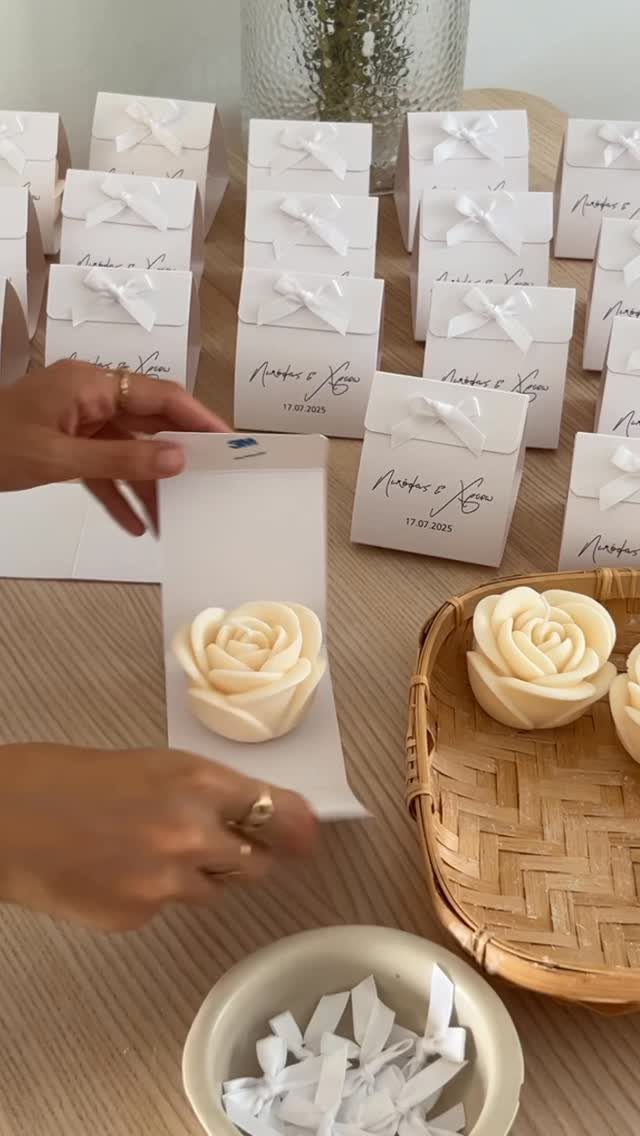 Rose-shaped cream candles being placed into small white gift boxes on a table.