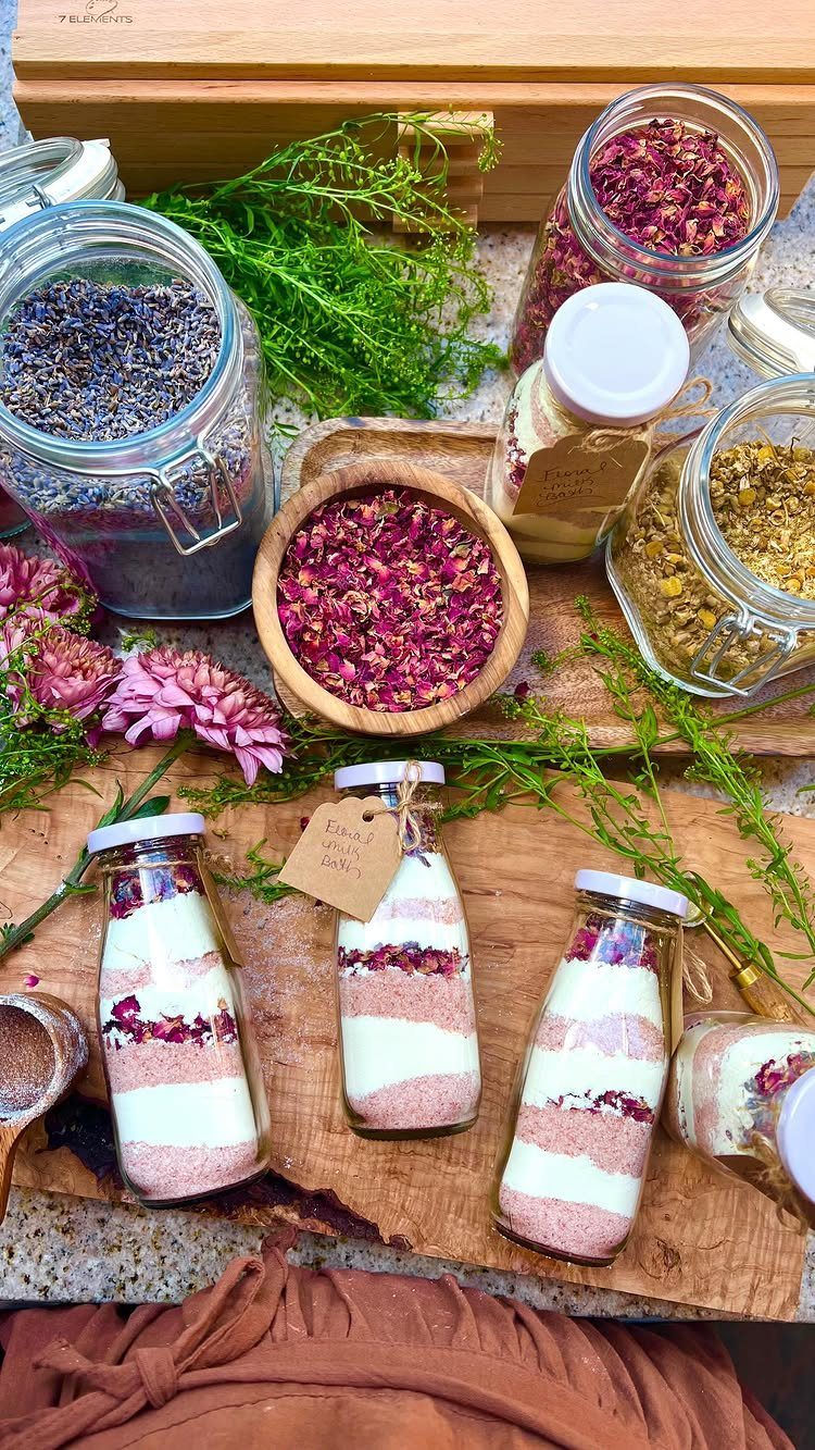 Layered pink and white bath salts in small bottles with dried flower petals.