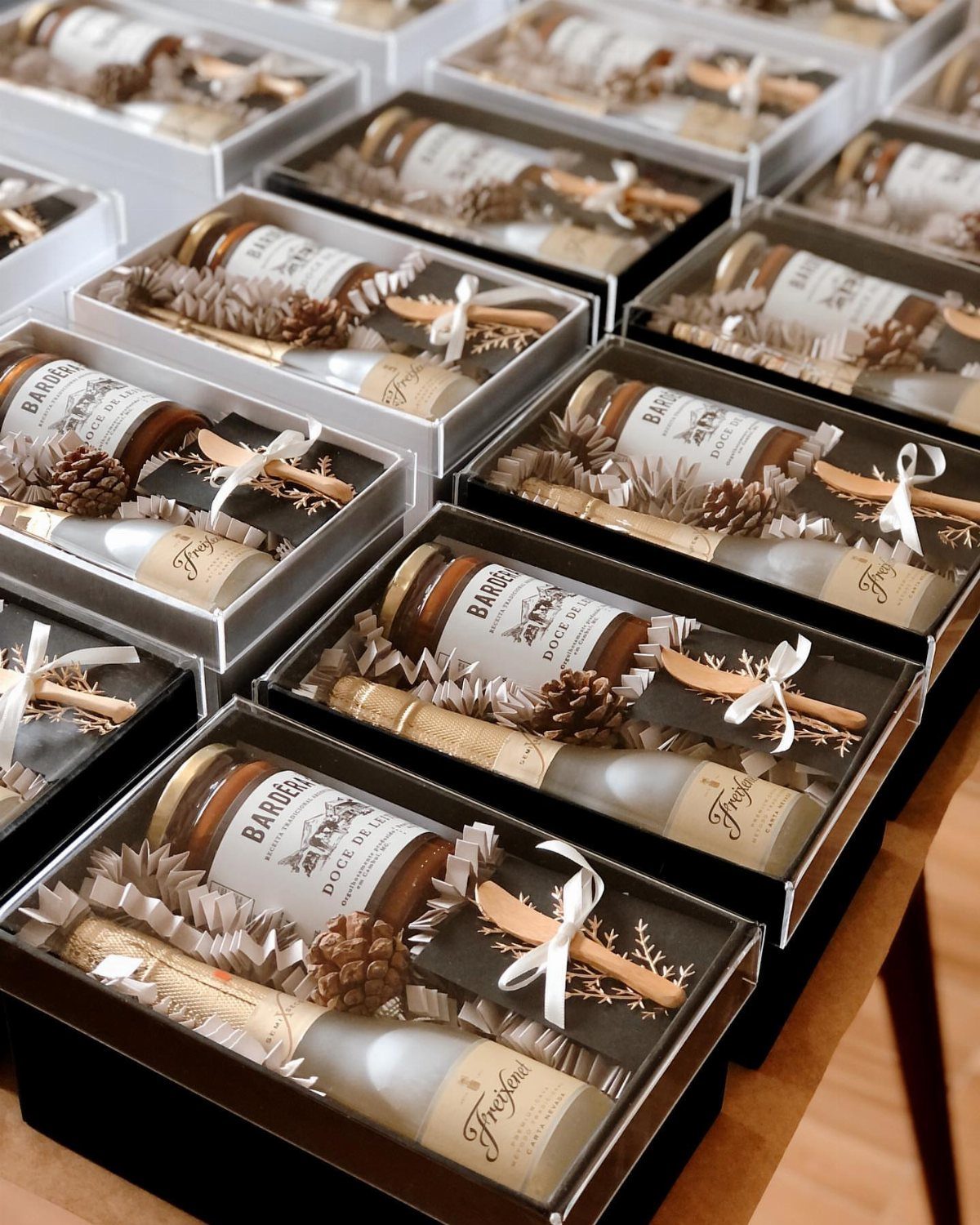 Mini bottles of wine and jam jars in white gift boxes with ribbons.