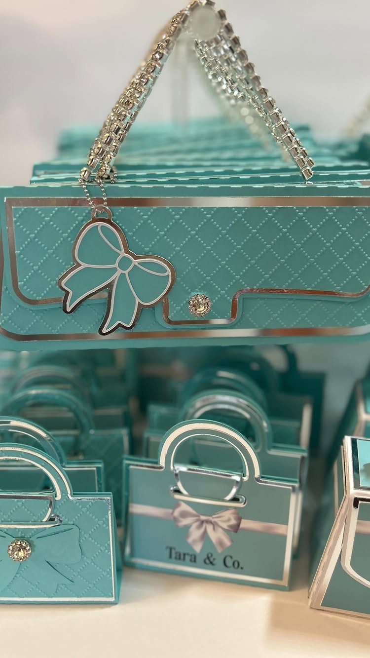Light blue handbag-shaped gift boxes with silver accents and bows for party favors.