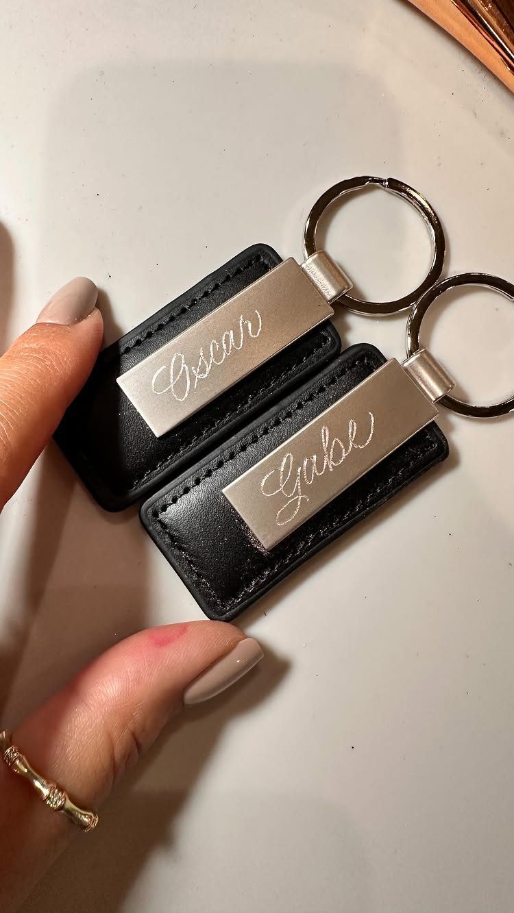 Two black leather keychains with silver plates engraved with the names Oscar and Gabe.